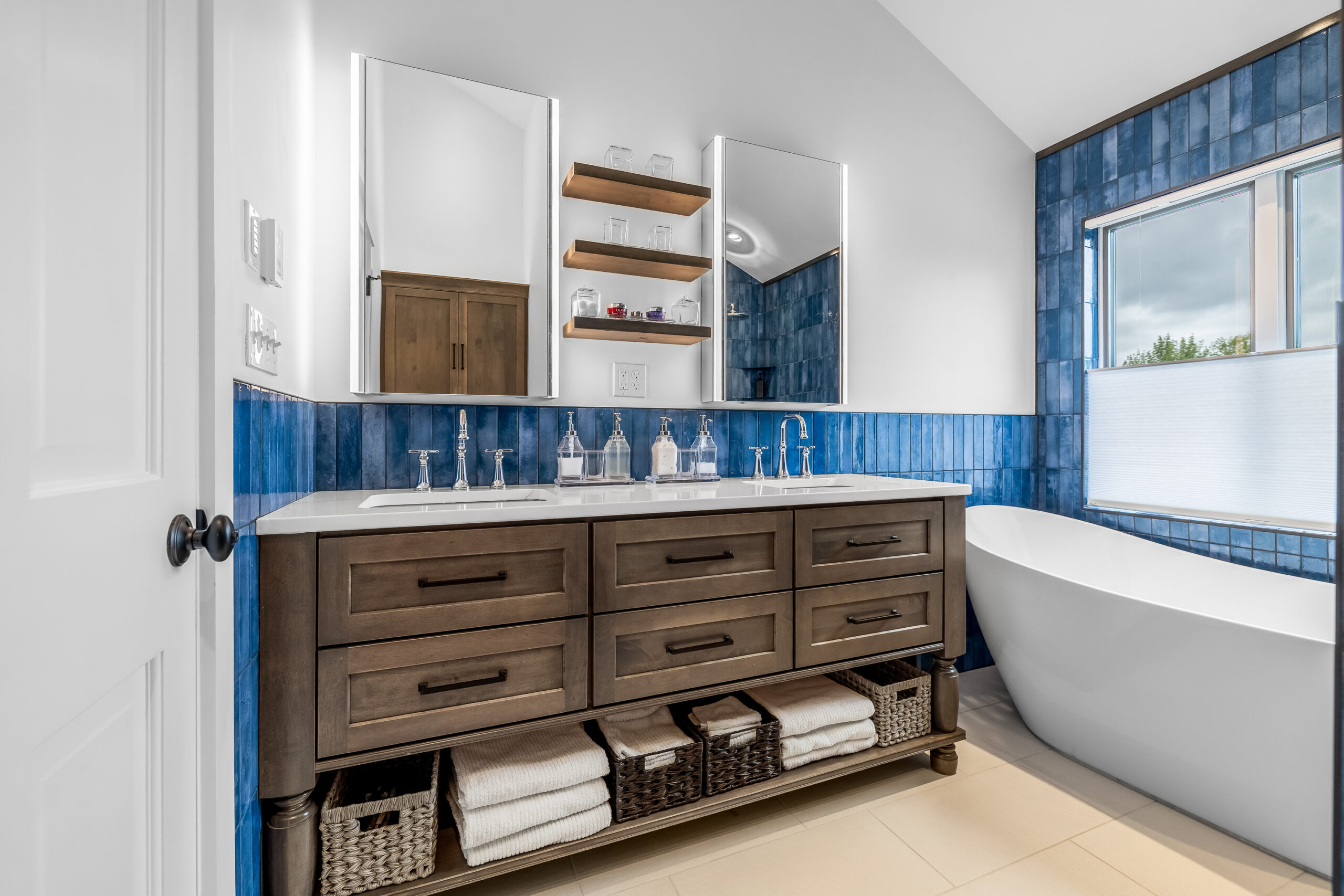 New Long bathroom remodel with blue tile, wood vanity with dark handles and freestanding soaker tub